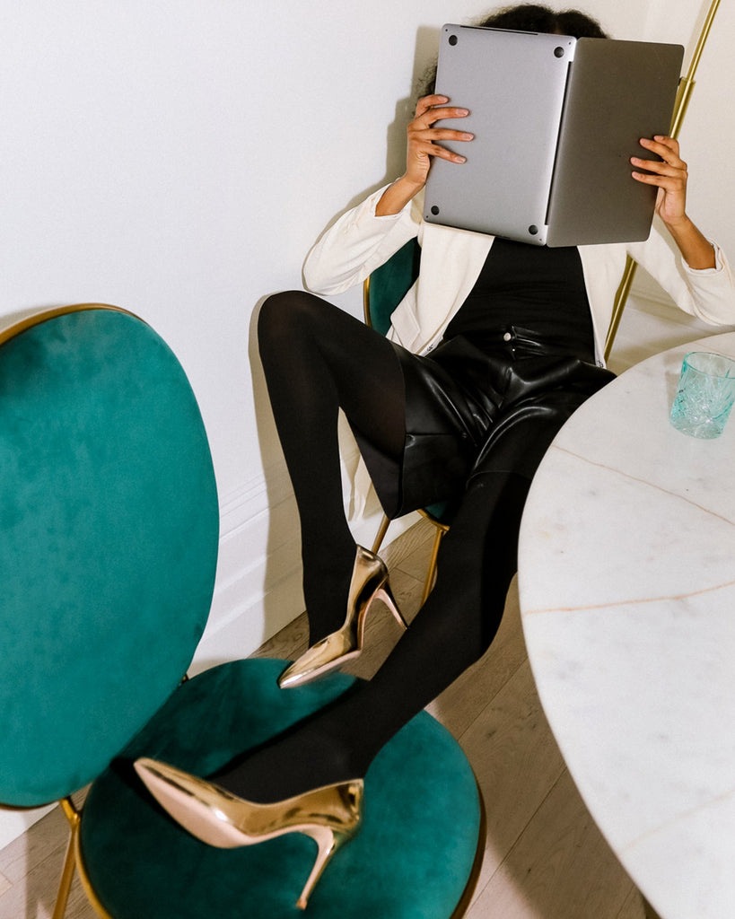 A person sitting on a chair in black opaque tights in 100 denier showing how to style 100 denier opaque tights for work and what shoes to wear with black opaque tights