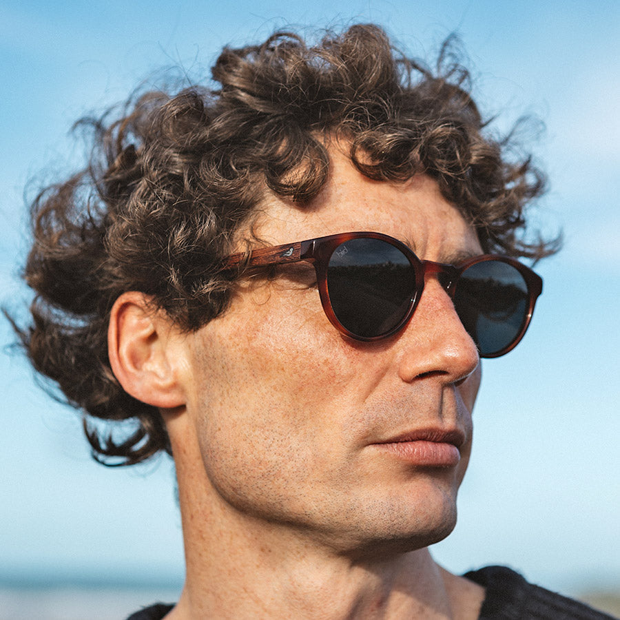 Man on beach wearing red bio acetate sunglasses with grey lenses