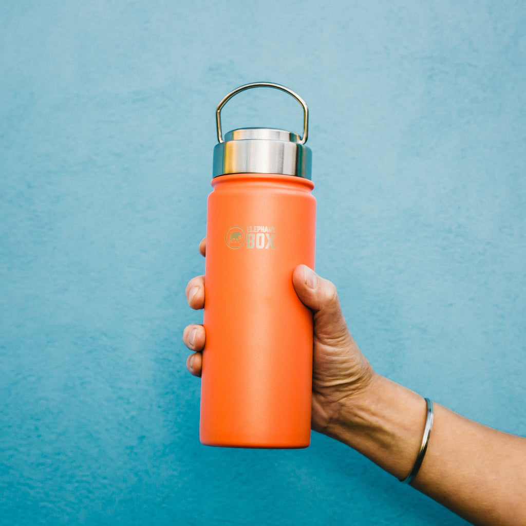 hand holding orange 500ml water bottle with carry loop against a a blue wall