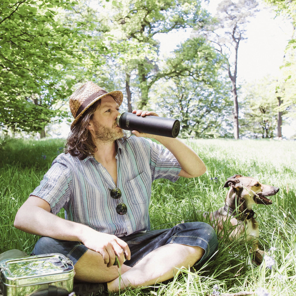 Man sitting in park with his dog drinking from a black water bottle